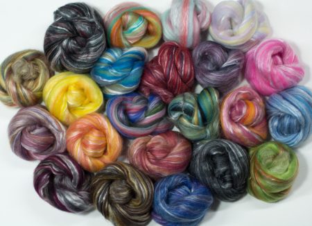 22 blended colorways of fiber wound into little nests and arranged on a flat surface for the picture.