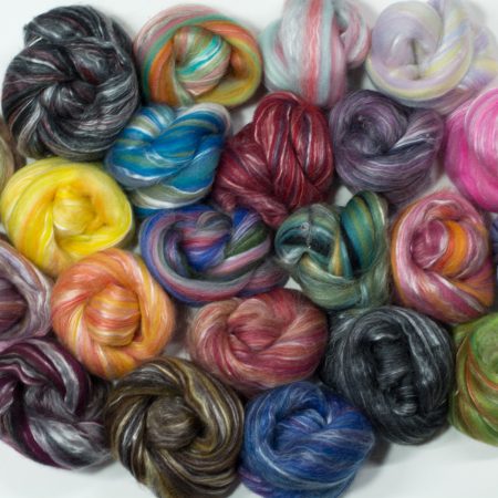 22 blended colorways of fiber wound into little nests and arranged on a flat surface for the picture.